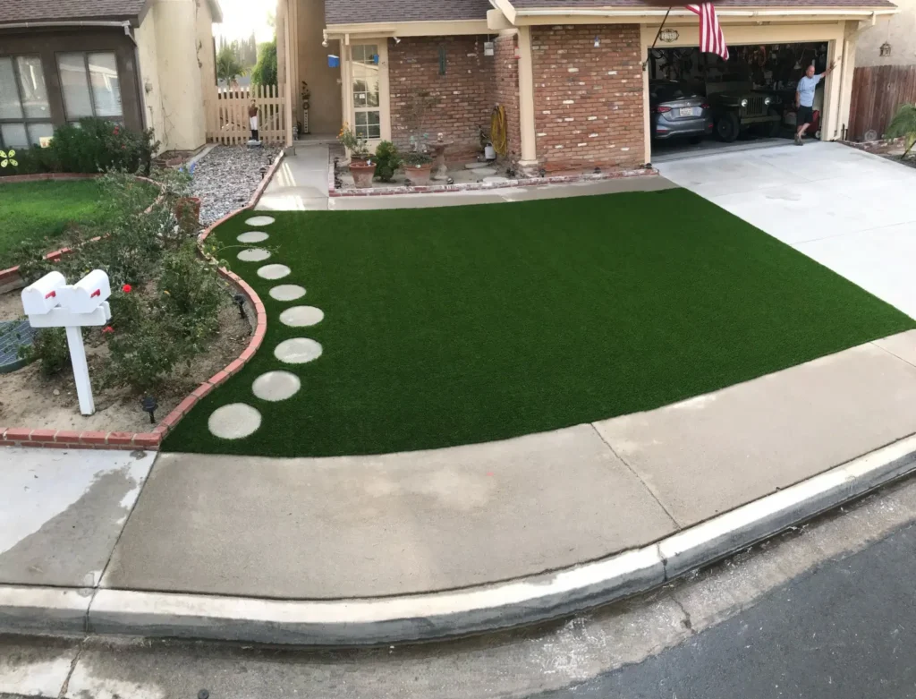 Front yard with synthetic grass and a decorative stepping stone path leading to a cozy house with a brick facade, under an open garage with an American flag.