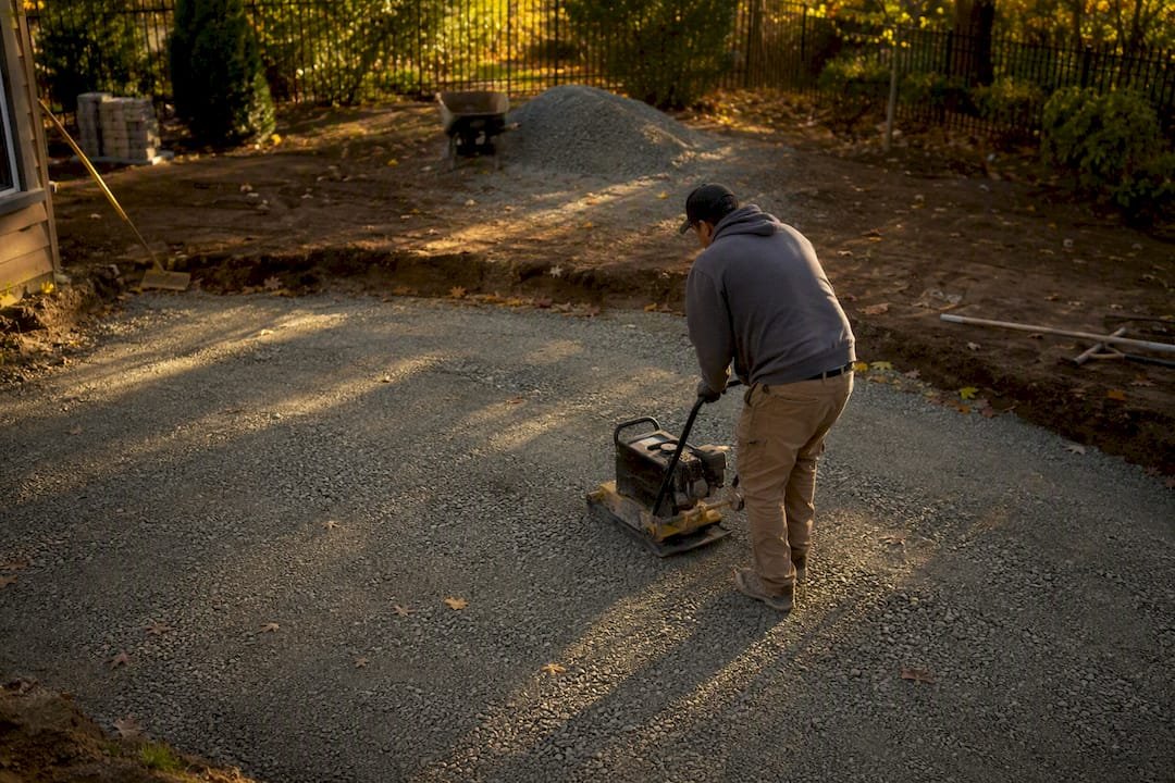 Worker compacting gravel base for pavers